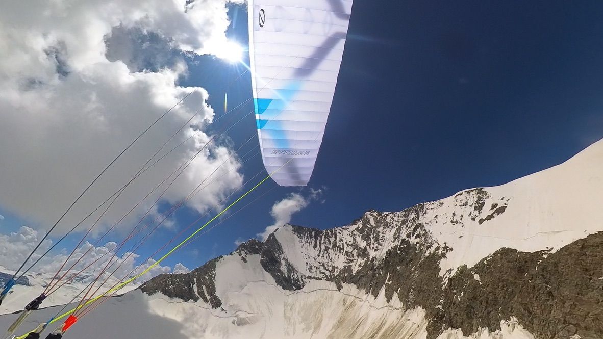 Paraglider wing flying above a glaciated ridge